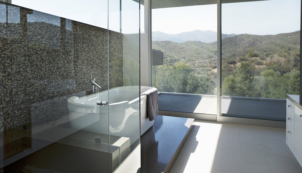 Salle de bain contemporaine avec baignoire îlot, paroi vitrée de douche et baie ouverte sur un paysage de collines